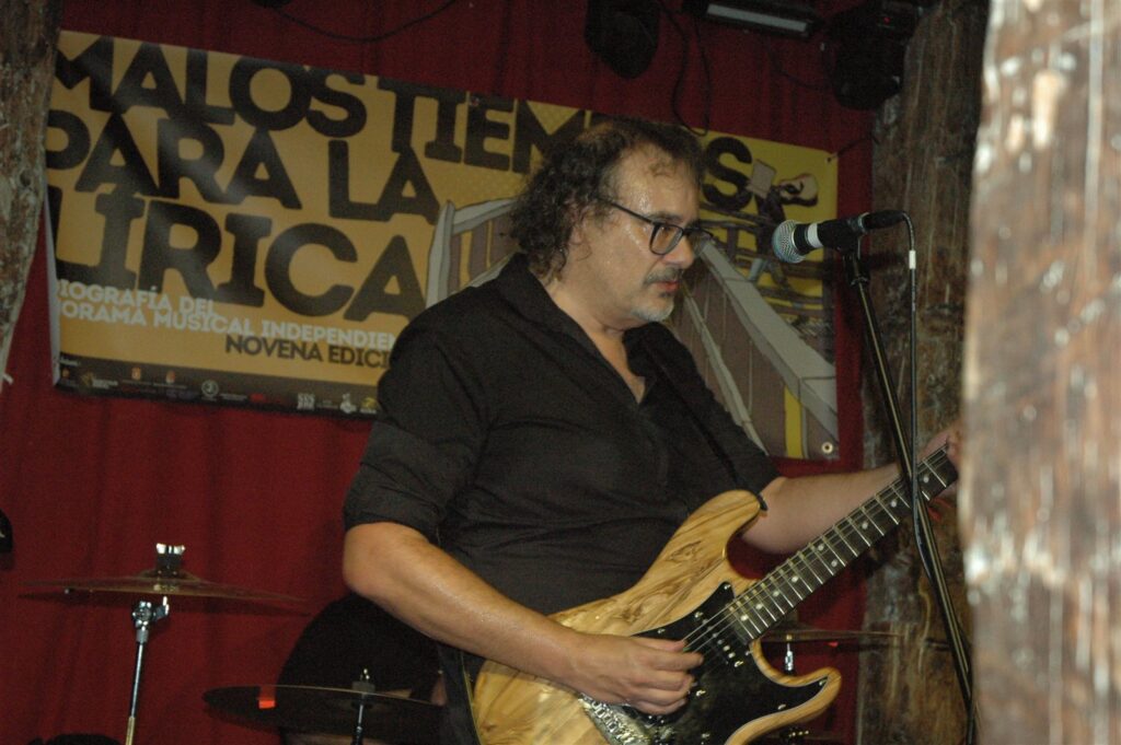 Guitarrista de Inspector Harry junto al cartel de Malos Tiempos para la Lírica en Los Clásicos